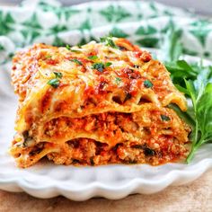 a white plate topped with lasagna covered in sauce and cheese next to greens