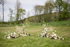 three flower arrangements in the middle of a grassy area with trees and bushes behind them