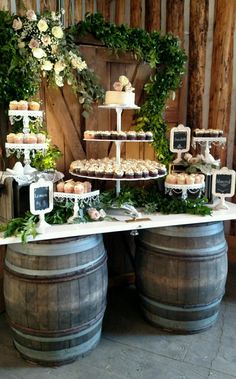 a table topped with cakes and cupcakes next to two barrels filled with wine