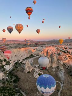 many hot air balloons are flying in the sky above some rocks and trees at sunset