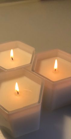 four lit candles sitting on top of a table next to each other in small square containers