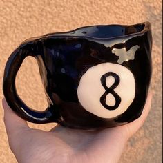 a hand holding a black and white ceramic eight ball mug