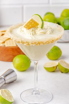 a margarita cocktail garnished with whipped cream and limes on a white counter