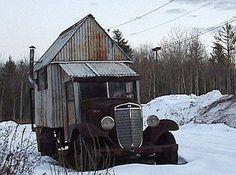 an old truck parked in the snow next to a small building with a shed on it