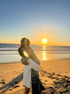 a man and woman hug on the beach at sunset