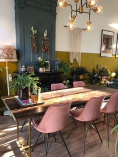 a dining room table with pink chairs in front of it and potted plants on the other side