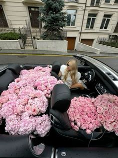 a woman sitting in the driver's seat of a car filled with pink flowers