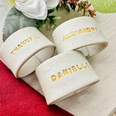 three personalized ceramic bracelets sitting on top of a wooden table next to flowers