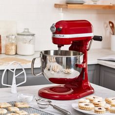 a red mixer sitting on top of a kitchen counter next to cookies and doughnuts