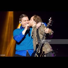 two men kissing each other while one is holding a guitar and the other has his mouth open