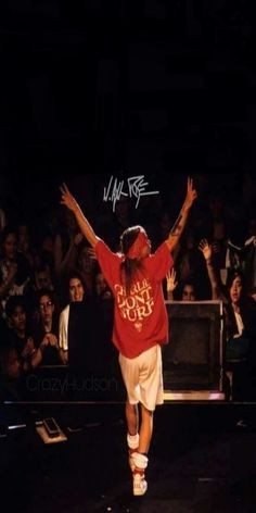 a man in red shirt and white shorts on stage with his hands up to the sky