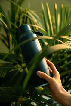 a person is holding a water bottle in front of some plants and palm tree leaves