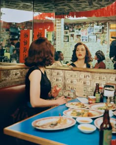 two women sitting at a table with plates of food on it in front of a mirror