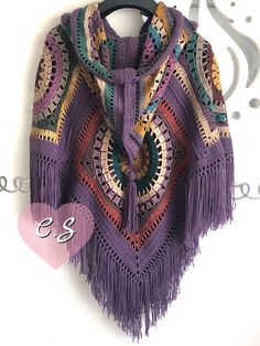 a purple crocheted shawl with fringes hanging on a hanger next to scissors