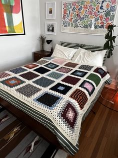 a bed with a quilt on top of it in a bedroom next to a painting