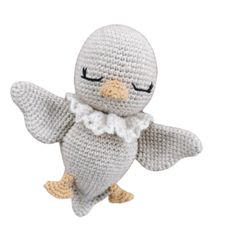 a crocheted stuffed bird with its eyes closed and wings spread out, wearing a white dress