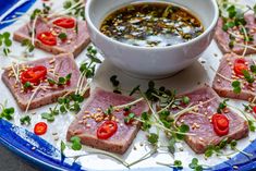 small pieces of meat on a plate with garnishes and sauce in a bowl