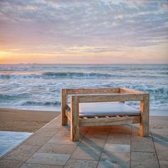 a wooden bench sitting on top of a tiled floor next to the ocean at sunset