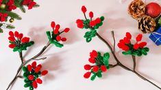 three branches with red flowers and pine cones on them, next to christmas balls and decorations