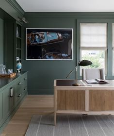 an office with green walls and wooden furniture in the corner, along with a painting on the wall