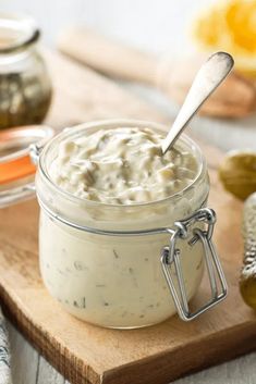 a jar filled with white sauce sitting on top of a wooden cutting board next to other food