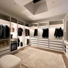 a large walk in closet with lots of clothes on the walls and shelves, along with a white ottoman