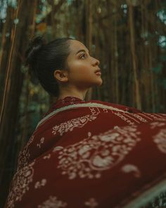 a woman wearing a red and white shawl in the woods with bamboo trees behind her