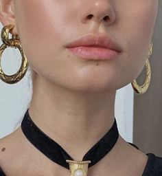 a woman wearing large gold hoop earrings and a black choker