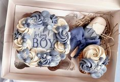 two cupcakes in a box decorated with blue and white icing, one has a boy on it