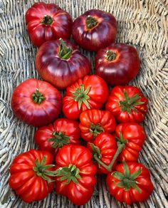 a basket filled with lots of red tomatoes on top of a woven table cloth covered in wicker