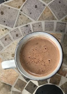 a cup of hot chocolate sitting on top of a tiled floor next to a black plate