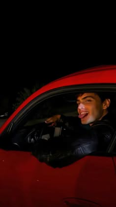 a man sitting in the driver's seat of a red car with his mouth open