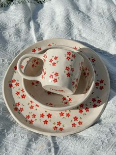 three cups and saucers sitting on top of a white cloth covered tablecloth with red flowers