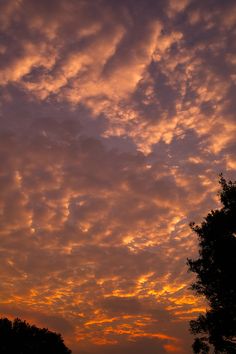 the sky is filled with clouds as the sun goes down in the distance behind some trees