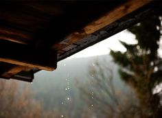 rain falling from the roof of a building in front of some trees and mountains behind it