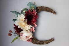 the letter c made out of twigs and flowers is hanging on the wall next to a white wall