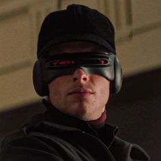 a man wearing a black hat and goggles with red eyes looking off to the side