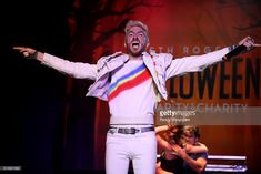 a man in white pants and jacket on stage with his arms spread out to the side