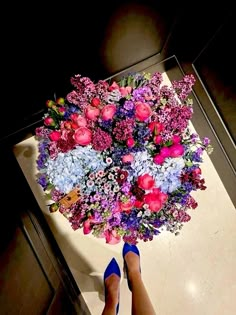 a woman's feet are standing in front of a bouquet of purple and blue flowers