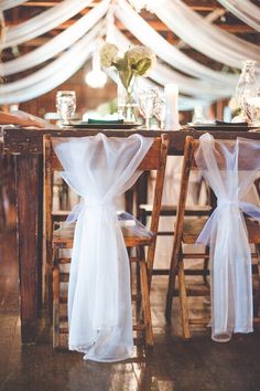 two wooden chairs with white sashes on them at a table set up for a wedding