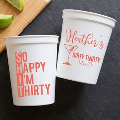 two white cups sitting next to each other on top of a wooden cutting board with limes