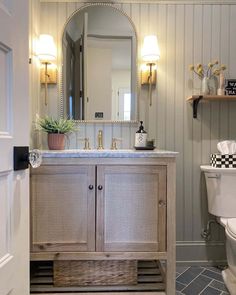 a white toilet sitting next to a bathroom sink under a mirror on top of a wooden cabinet