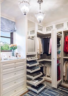 an open closet with clothes hanging on the shelves and drawers, in front of a window