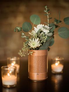 a vase filled with flowers and greenery sitting on top of a wooden table next to candles