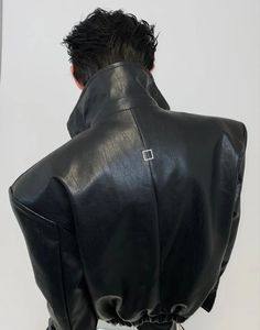 a man wearing a black leather jacket and white pants with his back turned to the camera