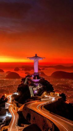 the statue of christ on top of a hill at night with city lights in the background