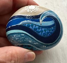 a hand holding a painted rock in the shape of a wave with white dots on it