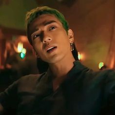 a young man with green hair and piercings on his ears looking at the camera