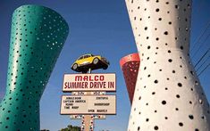 a yellow car is parked on top of a sign in front of some tall poles