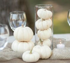 white pumpkins are stacked on top of each other in glass vases and candles